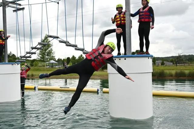 Sir Ed Davey wearing a life vest and yellow helmet falling into water