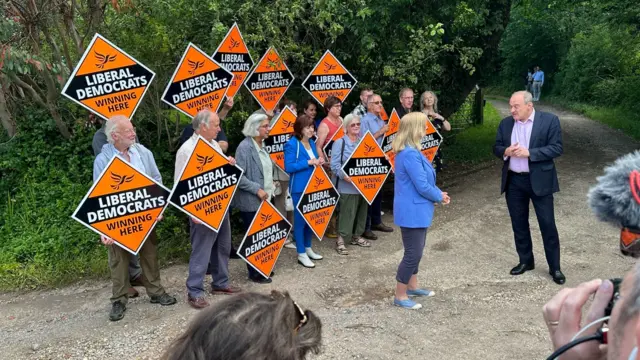 Liberal Democrat supports stand with diamond shaped signs saying Liberal Democrats winning here in front of Ed Davey