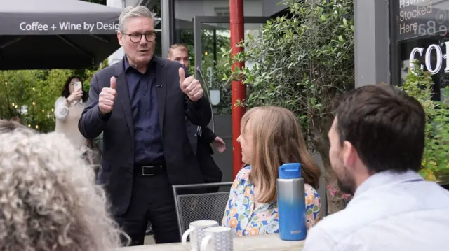 Labour Party leader Sir Keir Starmer (centre) gives a thumbs up to people sitting at a table in a bar during his visit..