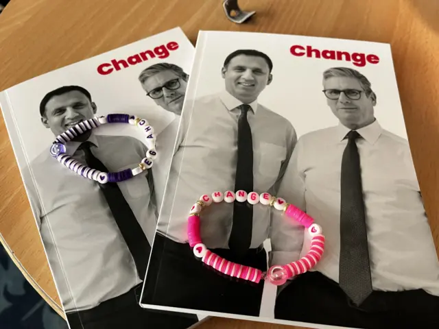 A purple and hot pink beaded friendship bracelet reading 'CHANGE' sitting on top of Labour's manifesto booklet