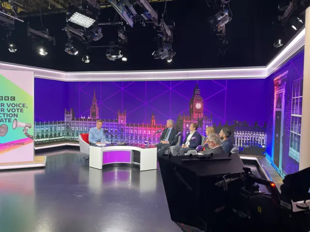 Dan O'Brien and the candidates sitting in a purple studio with cameras in the foreground