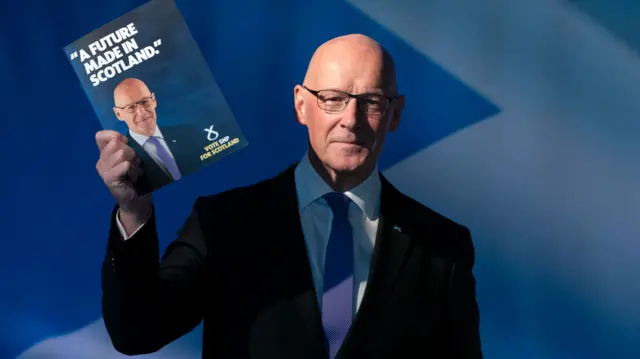 John Swinney holds up the SNP manifesto