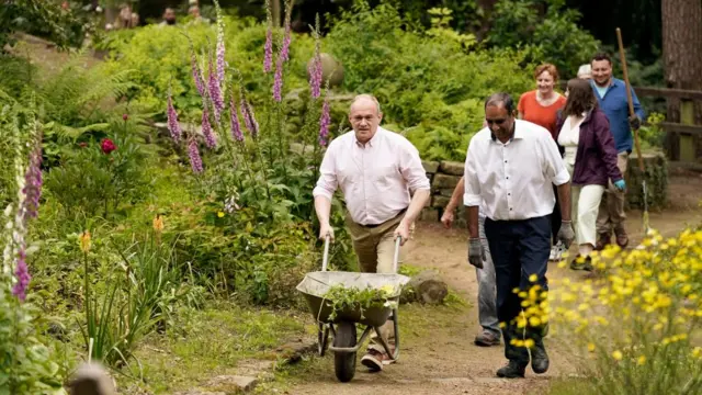 Ed Davey wheels a wheelbarrow while gardening