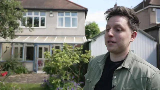 A man stands in back garden in front of a house