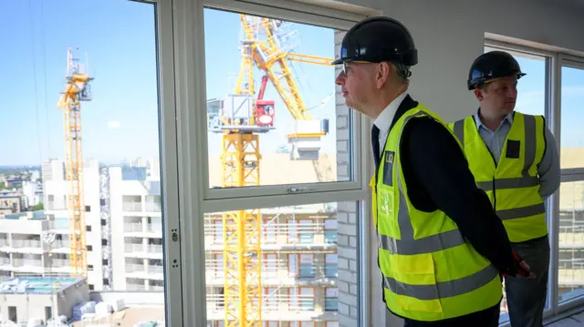 Michael Gove wears a hi-vis jacket while looking around a building site