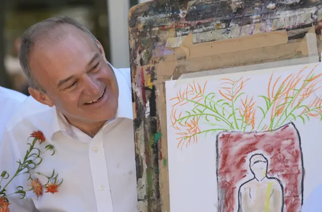 Ed Davey grins behind his drawing