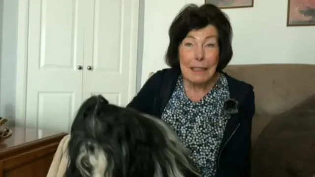 A woman sat on a sofa with a dog on her lap