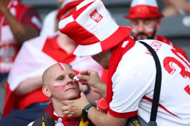 A fan helps another fan paint their teams' colours on their face