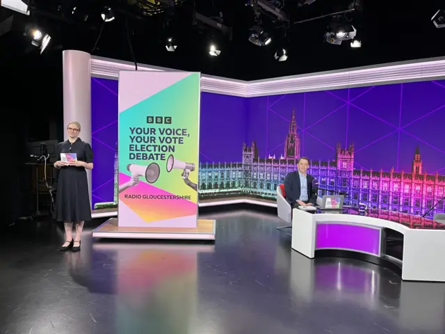 A woman standing and a man sitting in a large purple studio