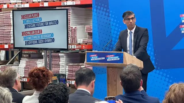 An image showing Prime Minister Rishi Sunak wearing a suit and addressing Welsh Conservatives from inside a warehouse