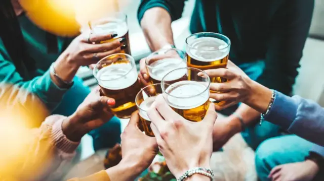 A picture of people giving cheers with glass cups filled with what appears to be beer or cider.