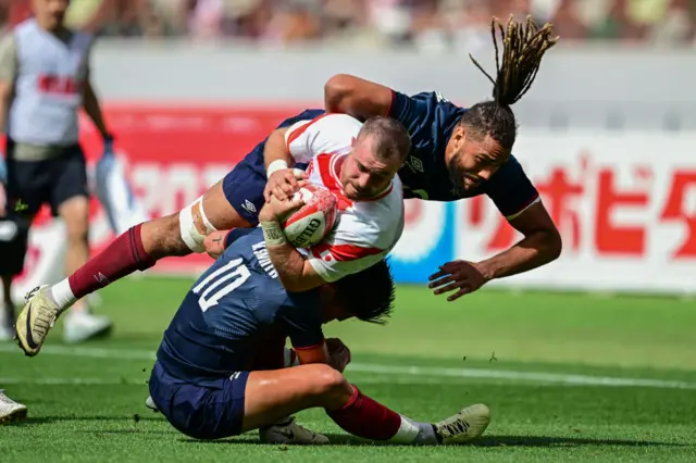 Japan's Tiennan Costley (C) is tackled by England's Marcus Smith (L) and England's Chandler Cunningham-South (R