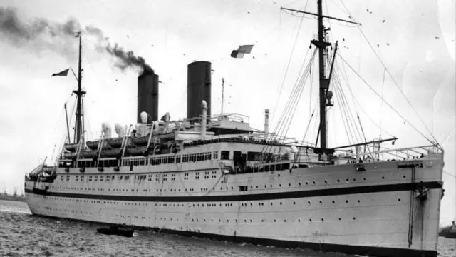 The Empire Windrush London - a large steamer ship - is seen in black and white on the water.