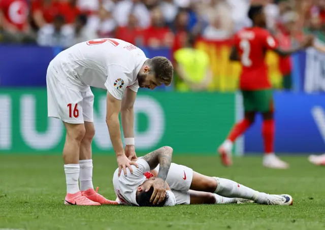 A teammate checks on Akaydin who lies on the floor after a challenge