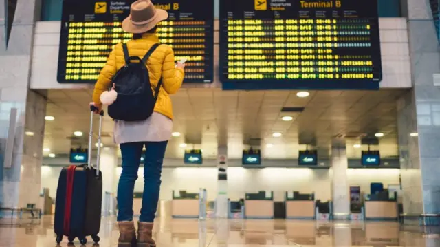 Woman looking at airport departure board (stock photo)