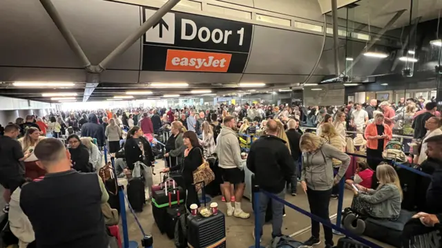 Passengers queue outside Terminal 1 after an overnight power cut led to disruptions and cancellations at Manchester Airport in Manchester, Britain