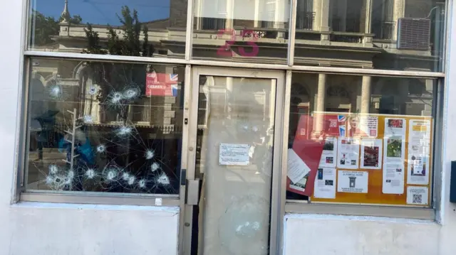 The left window and front door of Stella Creasy's office with several holes and cracks.