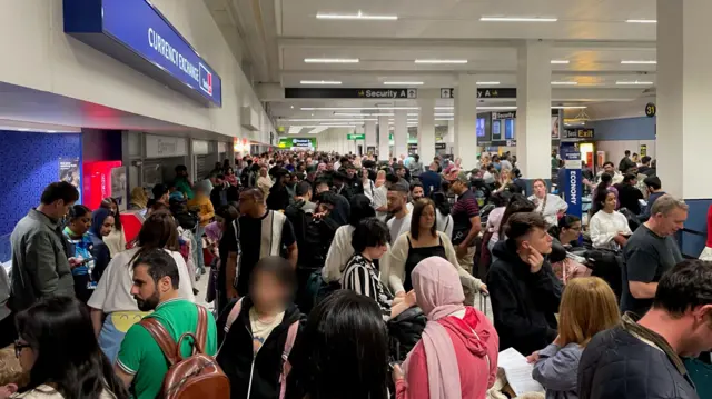 Passengers queue at Manchester airport following a power cut, that has caused flight cancellations and delays