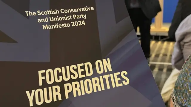 Blue Scottish Conservative manifesto held out in front of camera. It has the Union Jack pattern on the front.