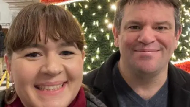 A selfie of Laura Saunders and Tony Lee in front of an artificial Christmas tree