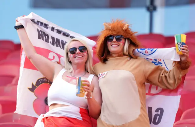 Fans stand inside the ground, one dressed as a lion, with the England flag