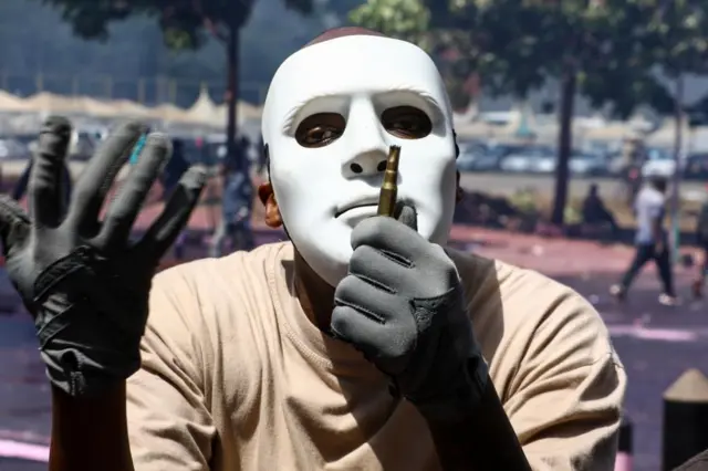 A masked demonstrator holds an empty ammunition shell used by police