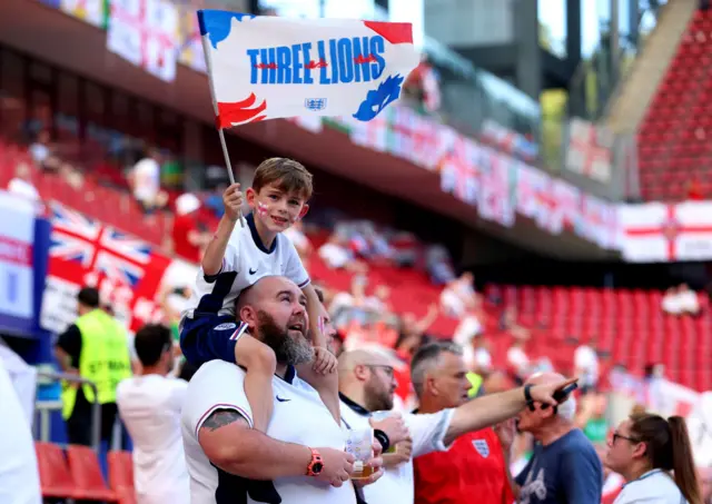 A young England fan sits on his Dad's shoulders and waves a flag