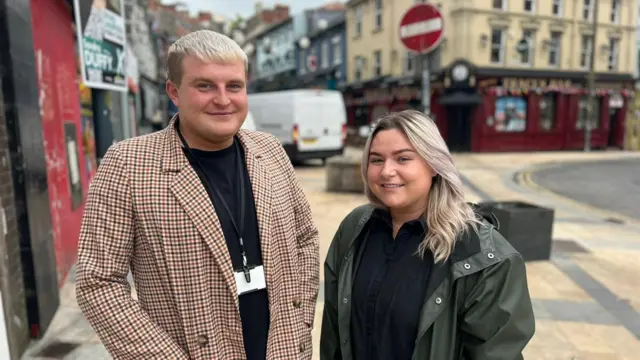 A male and a female standing side by side on a pavement