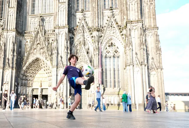 A young child plays football in front of Cologne Cathedral