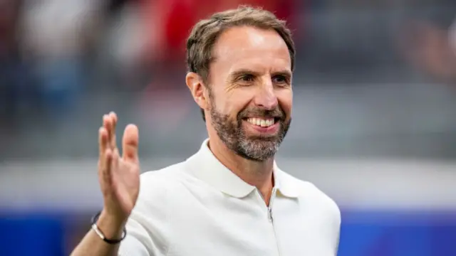England manager Gareth Southgate has a wide smile on his face.  He looks like he's about to high five someone.  He is wearing a white shirt
