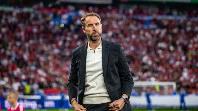 England manager Gareth Southgate standing in a stadium wearing a white shirt and navy blazer coach.