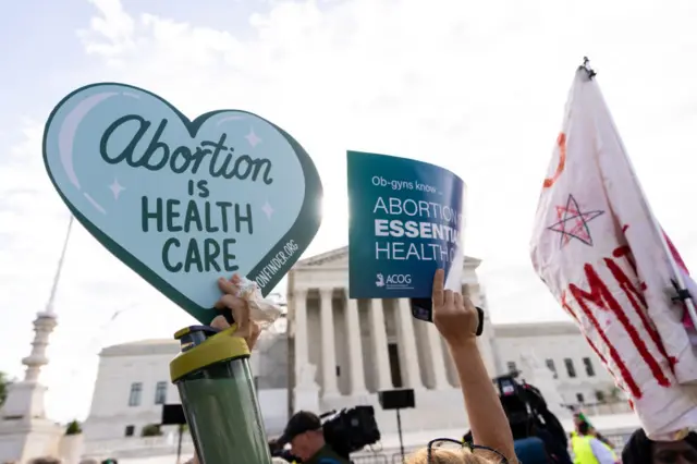 Demonstrators hold signs outside of the Supreme Court before the court's oral arguments in Moyle v. United States in Washington on Wednesday, April 24, 2024.