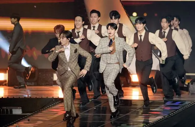 The K-pop band Seventeen, dressed in tweed, beige suits, skip down the runway of a stage in unison