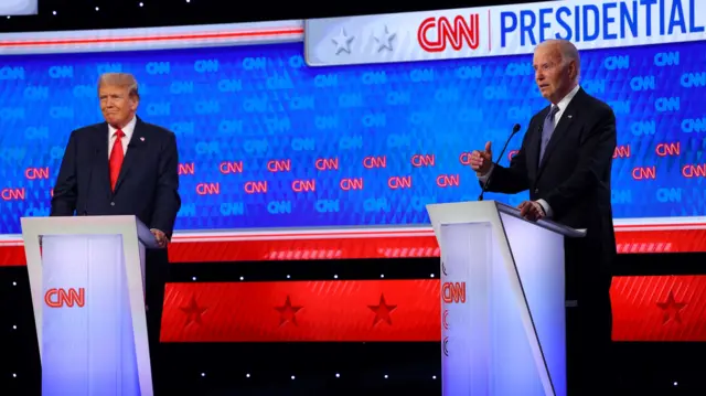 President Joe Biden, right, motions with his hand as he answers a question. Donald Trump is seen on the left slightly smiling.