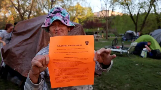 An unhoused woman named Kimberly Morris holds up a notice a police officer gave her giving her 72 hours to move her tent from the park, in Grants Pass, Oregon, U.S, April 18, 2024