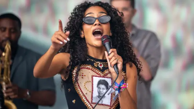 Olivia Dean performs on the Pyramid Stage at Glastonbury Festival dressed in a black tank top with colourful wristbands