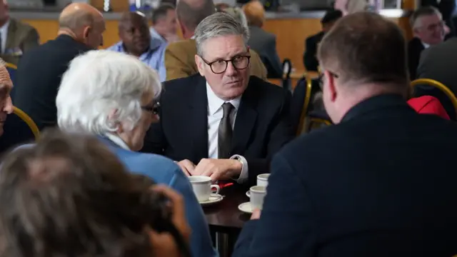 Sir Keir Starmer talking to veterans with cups of coffee