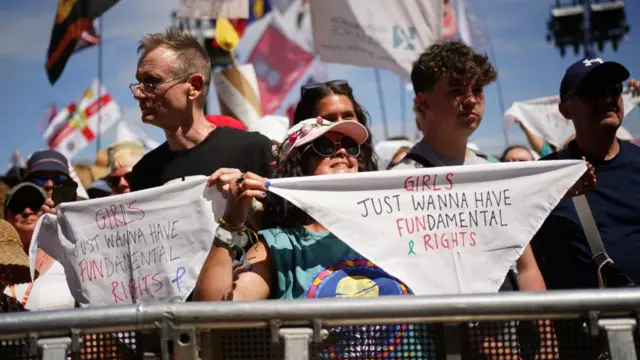 A little girl, smiling, holds up a sign that says "Girls just wanna have fundamental rights"