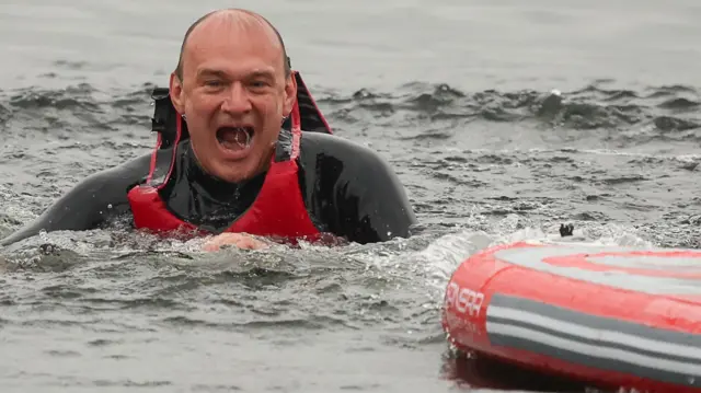 Ed Davey wearing a life jacket in water next to a paddleboard