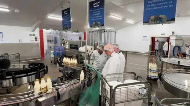 A wide shot of John Swinney watching operations at a dairy with two others