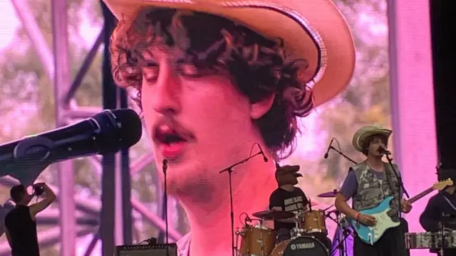 Fat Dog performs on stage with a guitar. A screen behind the leader singer shows him