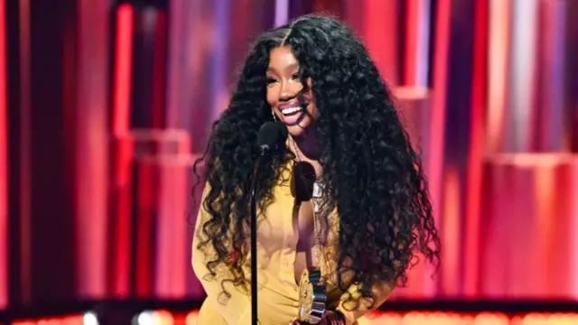 SZA in a yellow dress in front of a red background