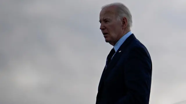 US President Joe Biden is seen against a cloudy sky