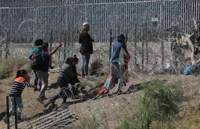 Migrants wait between barbed wire near the US border wall, in Ciudad Juarez