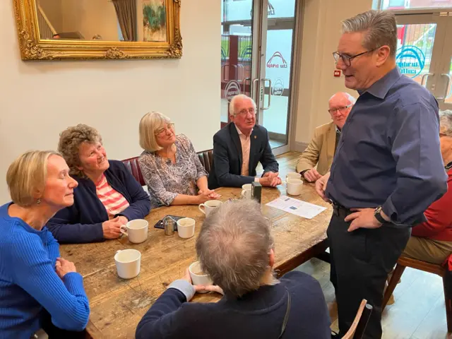 Labour leader Keir Starmer talks while to pensioners sitting down at a wooden table in a café in Bolton