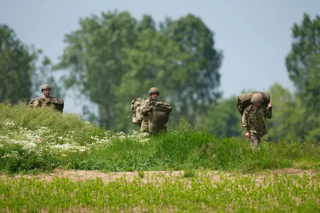 Paratroopers carry their parachutes in the fields of Caen