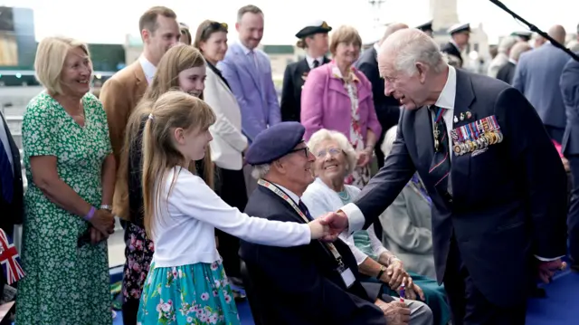 King Charles III shakes the hand of a young female family member of a veteran