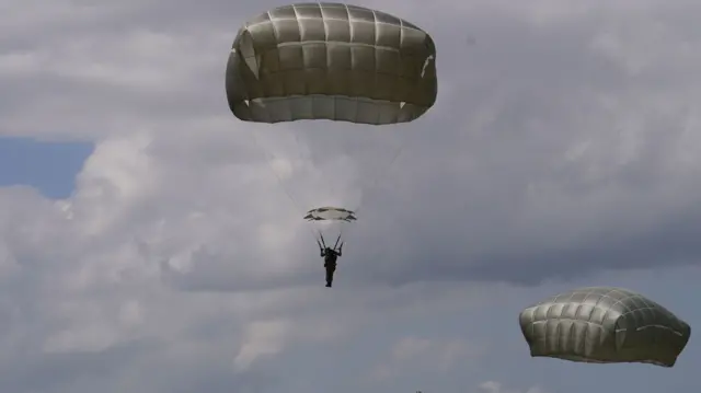 Military personnel descend to the ground in open parachutes