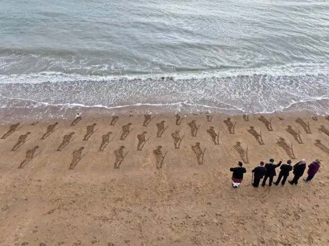 Veterans standing to attention behind sand art installation of soldiers. Drone shot taken in Broadstairs