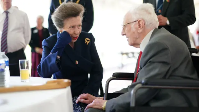 Princess Anne rests her face on her gloved hand as she chats to a veteran in a wheelchair